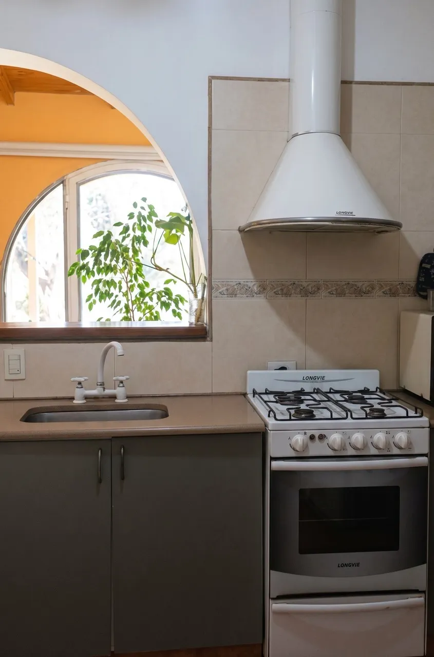Cocina con una ventana en arco, mesada con bacha y cocina a gas con horno y campana.