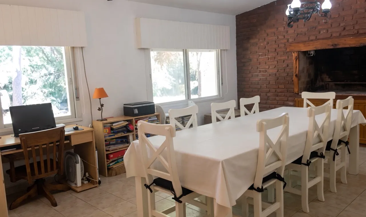 Comedor con mesa larga, sillas blancas y una pared de ladrillo con hogar.