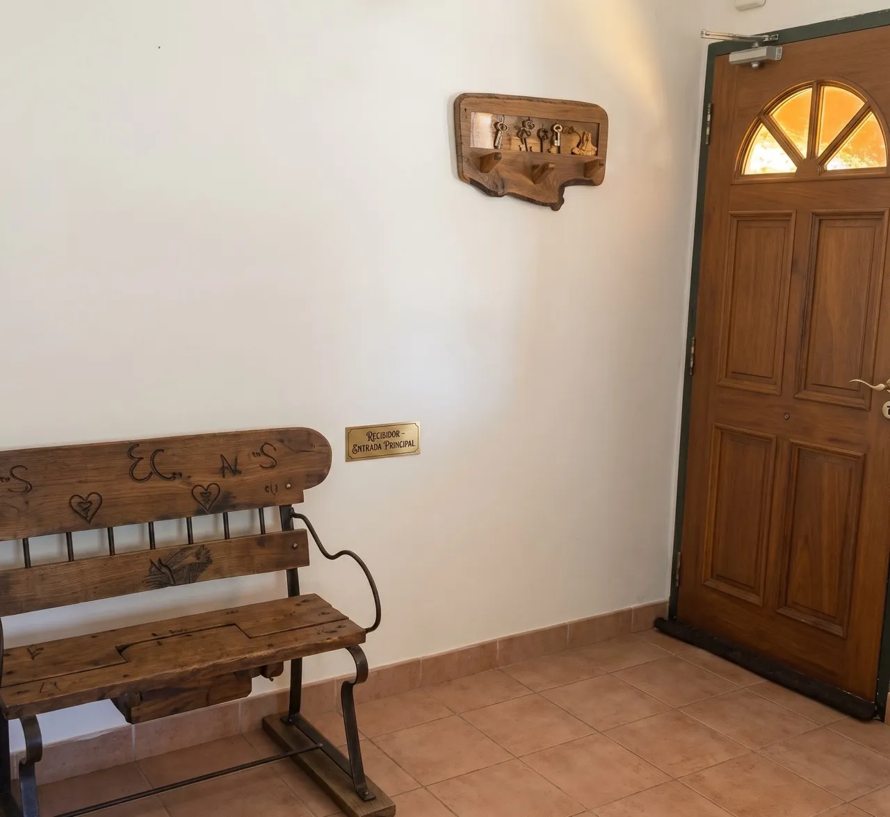Recibidor con puerta de madera con vidrio en abanico, un banco rústico y un perchero de madera.