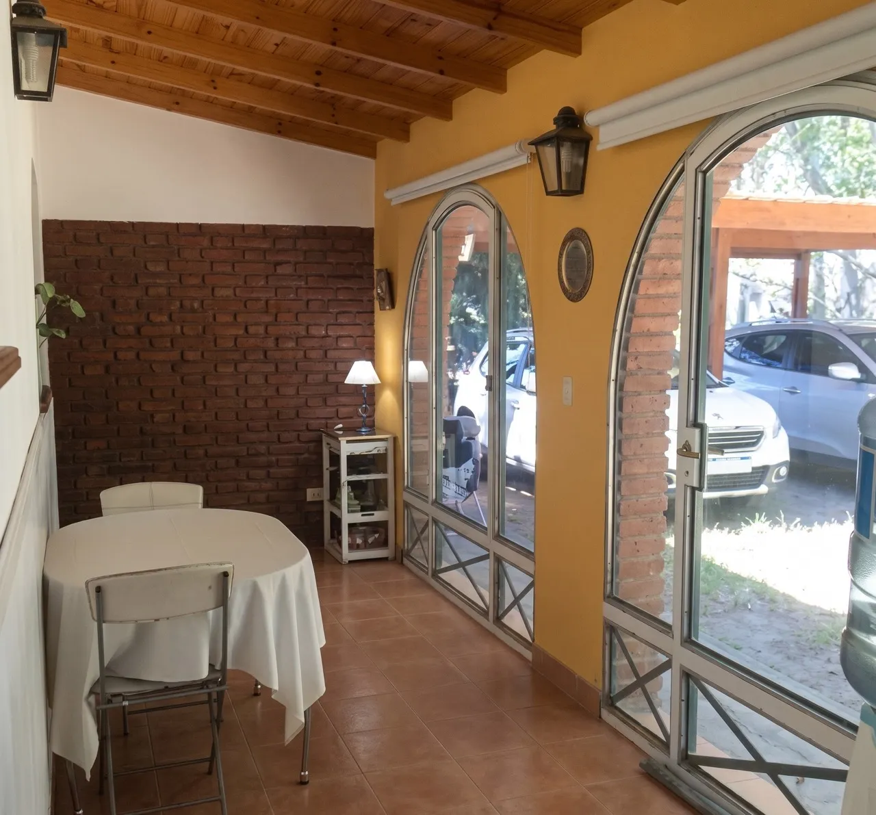 Sala con ventanales en arco, pared de ladrillo, cielorraso de madera y una mesa redonda.